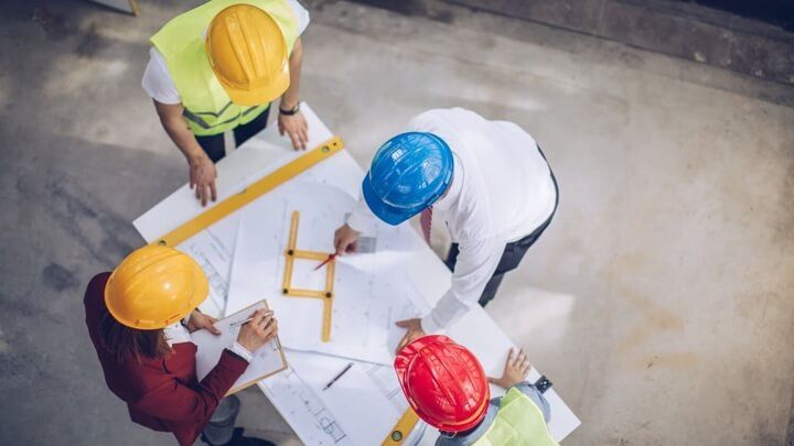 Overhead shot of a four people examining a plan on a building site.