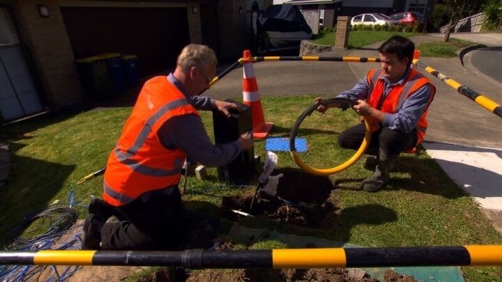 A photo two technicians installing fibre near a street.